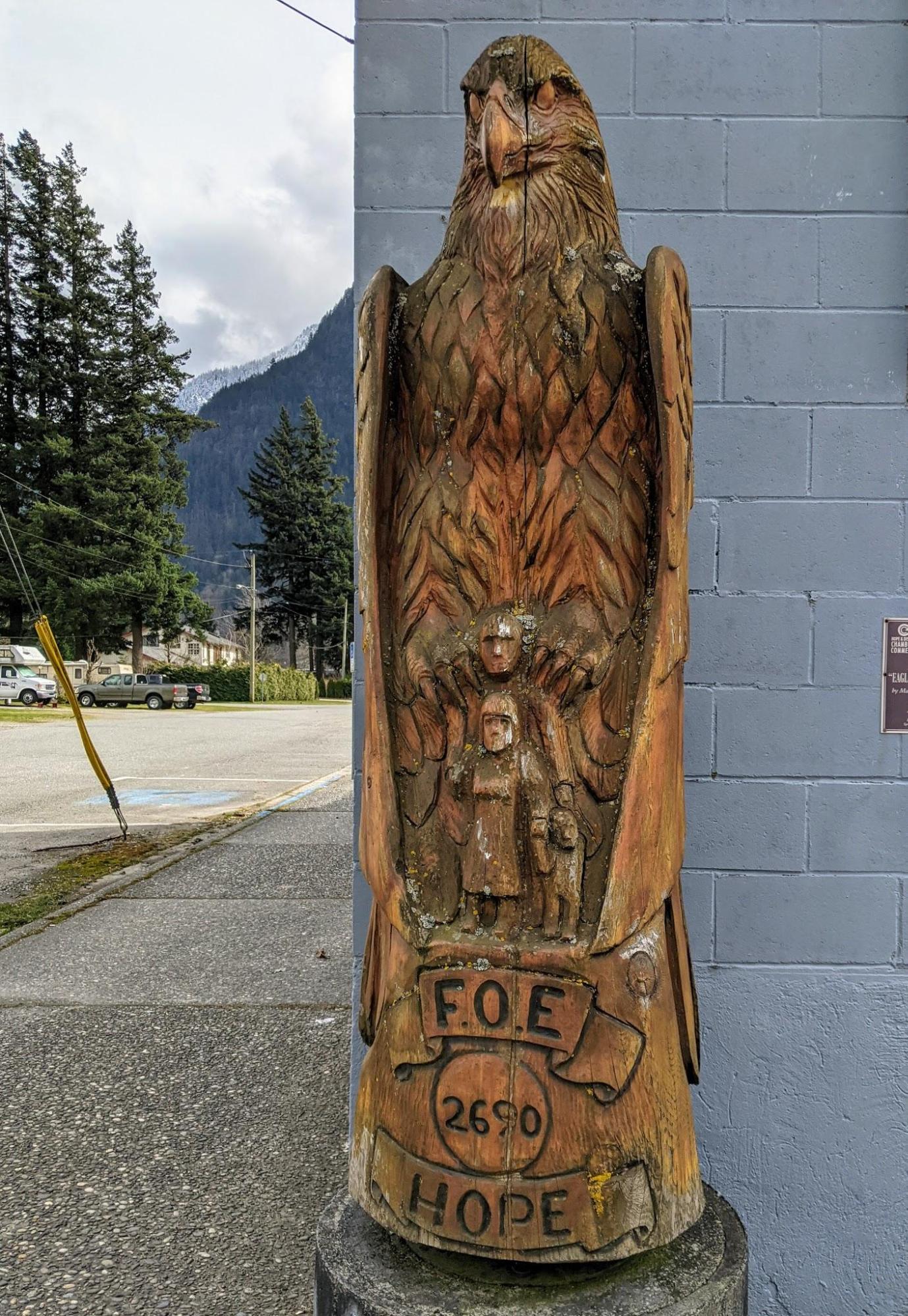 Chainsaw carving by master carver Pete Ryan of a large eagle sitting on a man's shoulders sheltering the man and his family with it's wings. Carving on display in the town of Hope, British Columbia, Canada 