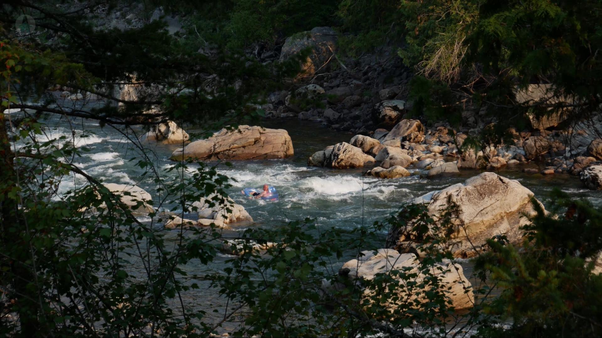 A person riding the small rapids on the Similkameen River from the comfort of a water floaty at Old Hedley West Recreation Site. 