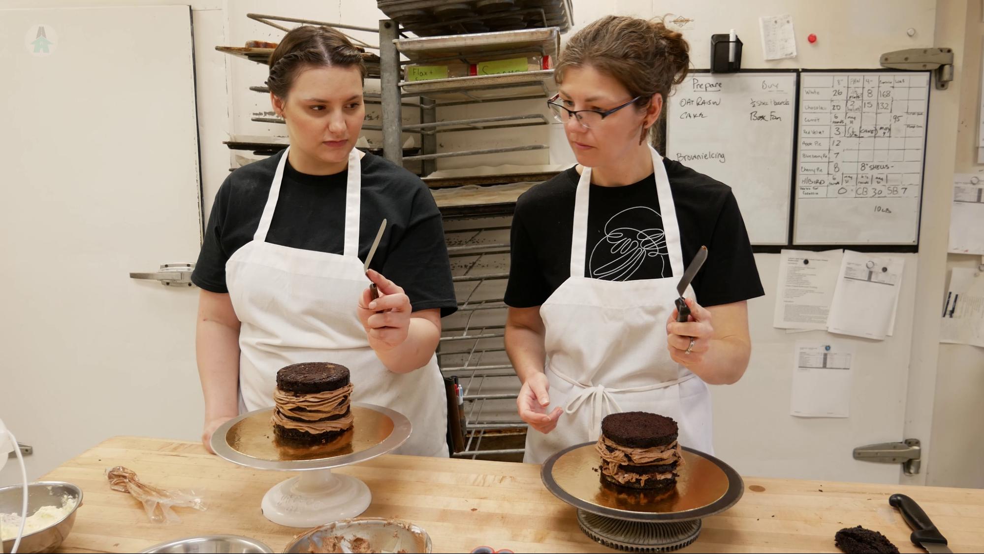 Cara shows Mel how to hold a cake spatula for icing a cake.